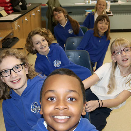 A group of students in blue and white uniforms pose for a picture, they alternate leaning from left to right while sitting in a row.