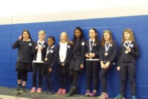Young students line up together against a blue brick wall with award medals