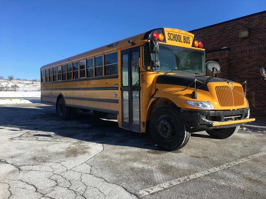 A yellow school bus parked on pavement beside brick school building