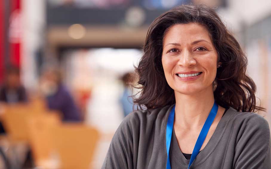 Smiling woman wearing a lanyard, standing indoors with a blurred hallway background.