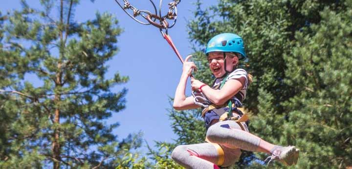 young girl on a zipline with pine trees and a blue sky behind